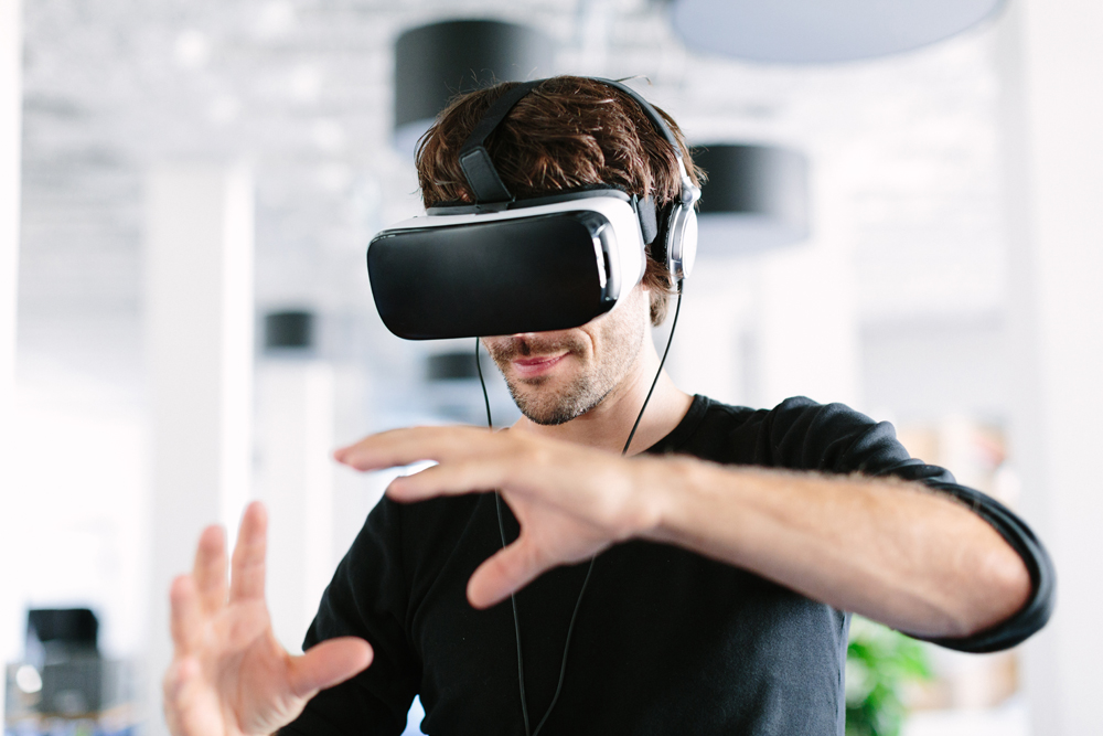 Young man wearing virtual reality glasses and gesturing in office
